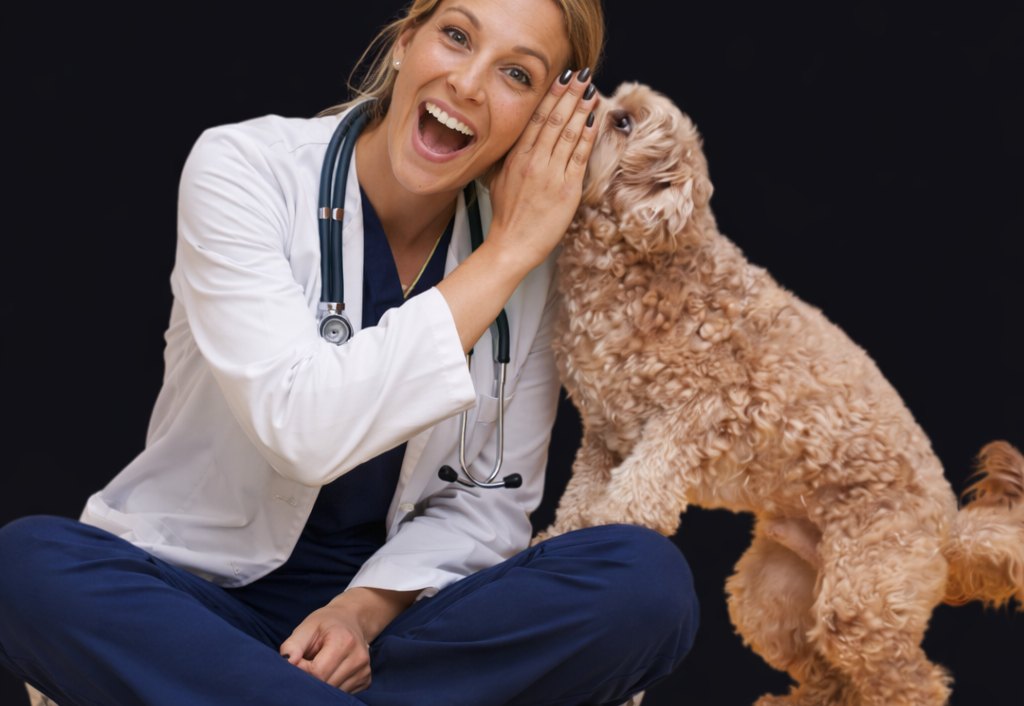 A veterinarian sitting on the floor with a cockapoo leaning into her face